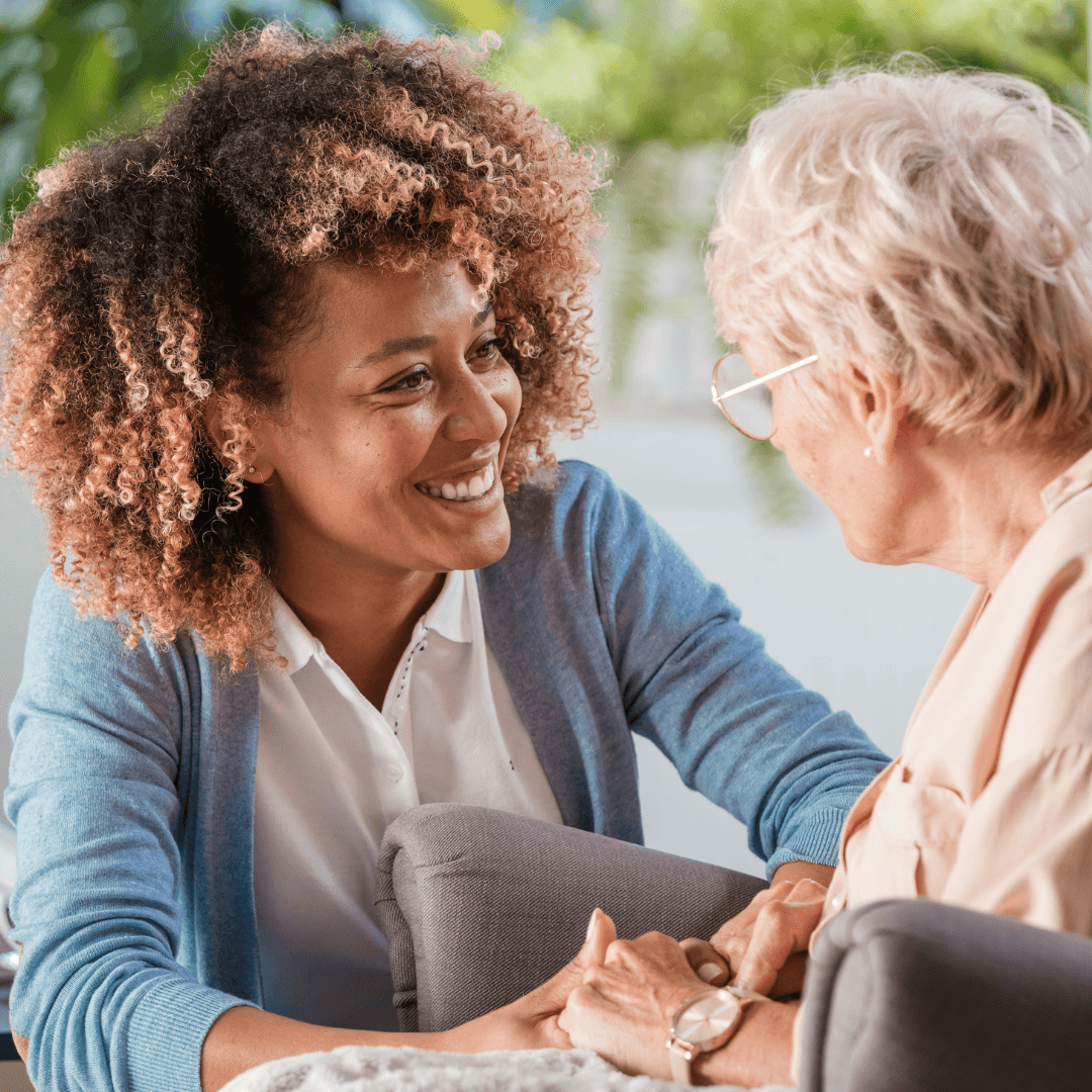 A smiling caregiver holding hands with an older woman in her home
